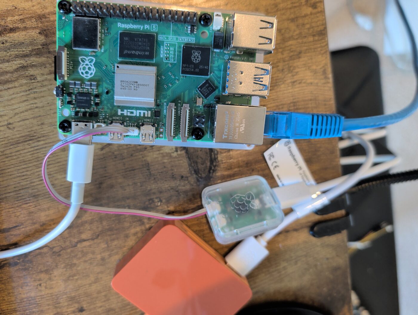 Raspberry Pi 5 on a workbench, Broadcom BCM2712 and RP1 southbridge visible, with a Raspberry Pi Debug Probe wired to the UART header and an ethernet cable attached